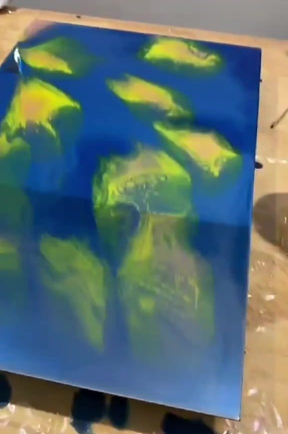 Espelho retangular coberto de azul profundo com manchas amarelas, sobre a bancada do ateliê.