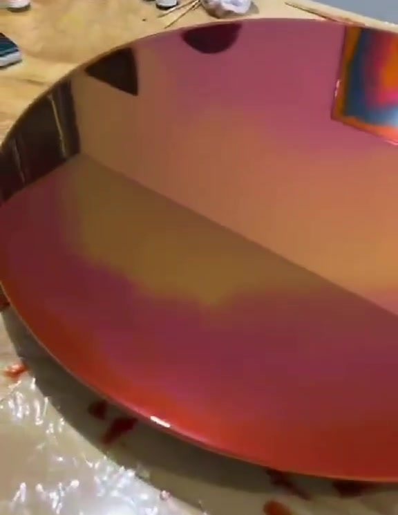 Espelho redondo em degradê de vermelho e âmbar, refletindo o ateliê.